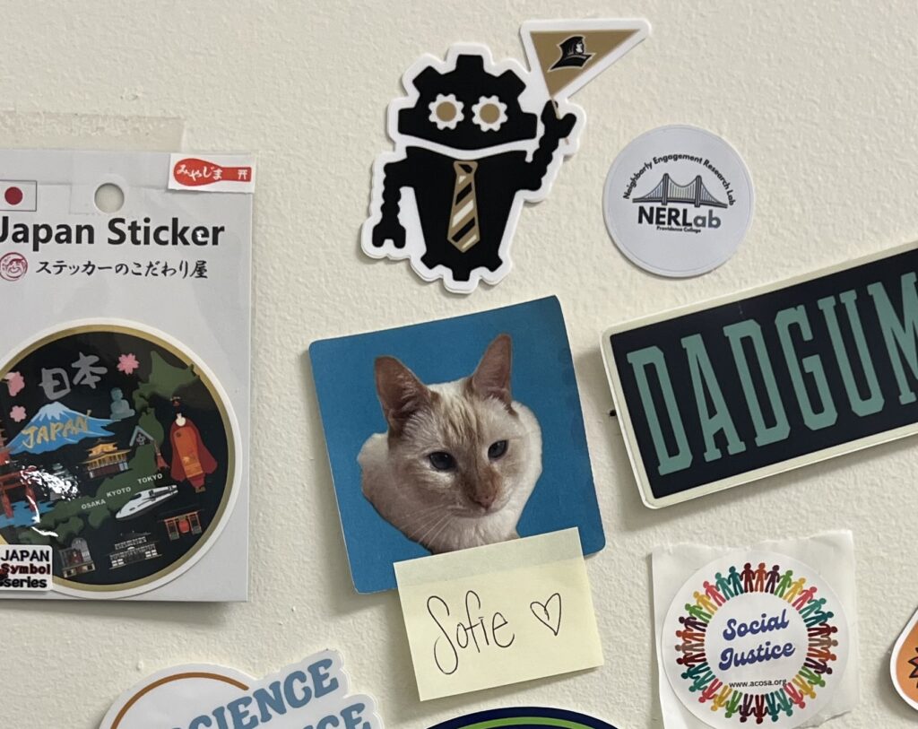 Providence College DubBot sticker sits above a collection of other stickers, including one of a Siamese- like cat named Sophie.