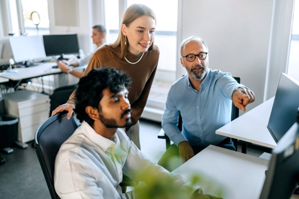 Three people looking at a computer screen, pointing and discussing